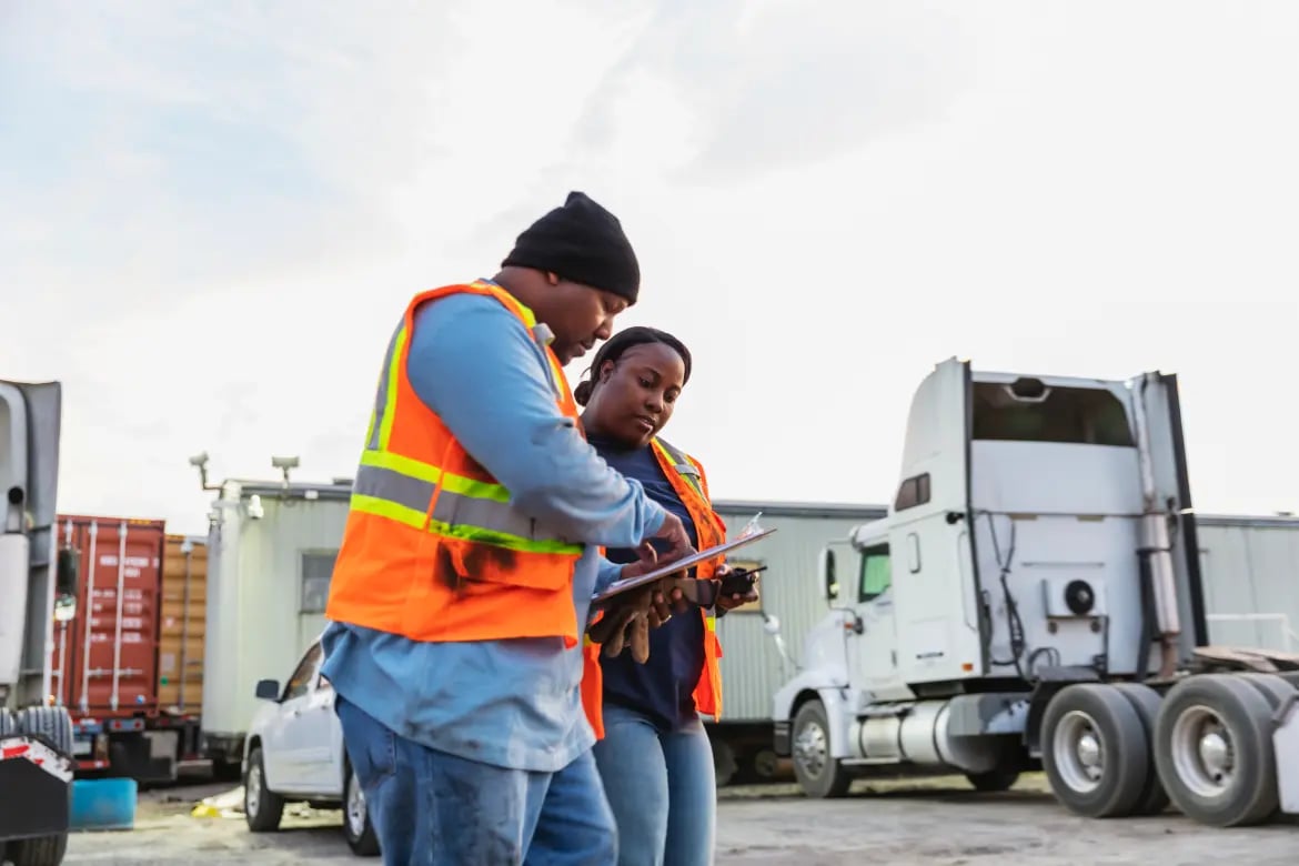 Two workers in safety vests reviewing forms on a clipboard on a worksite